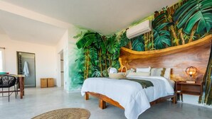 A bedroom with a bed, a nightstand, a lamp, a woven rug, and a wall mural of tropical foliage. - La Casa Blanca (Puerto Vallarta)