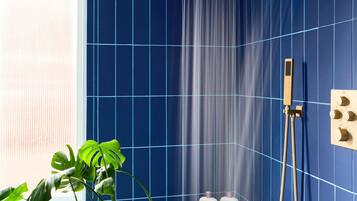 Une salle de bain avec des murs recouverts de carreaux bleus, une pomme de douche, un pommeau de douche amovible et une plante en pot.