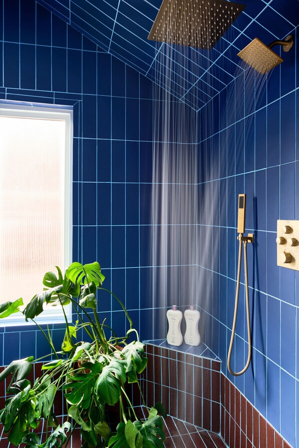 Une salle de bain avec des murs recouverts de carreaux bleus, une pomme de douche, un pommeau de douche amovible et une plante en pot.