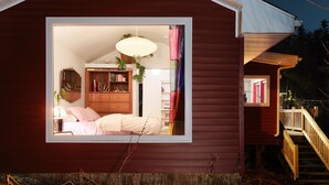 Une chambre confortable avec une grande fenêtre, une commode en bois et un luminaire suspendu.