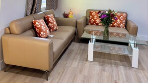 Een woonkamer met twee banken, een glazen salontafel, een decoratieve krans en een bijzettafeltje met een lantaarn.