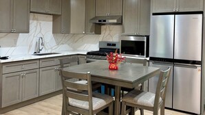 Een moderne keuken met grijze kastjes, een roestvrijstalen koelkast, een inbouwoven en een eettafel met stoelen.