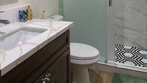 Een badkamer met een glazen douchecabine, een wit toilet, een marmeren wastafelmeubel en een spiegel.
