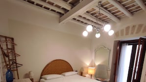 Una camera da letto con soffitto in legno, un letto con biancheria bianca, un comodino con una lampada e un pavimento decorato.