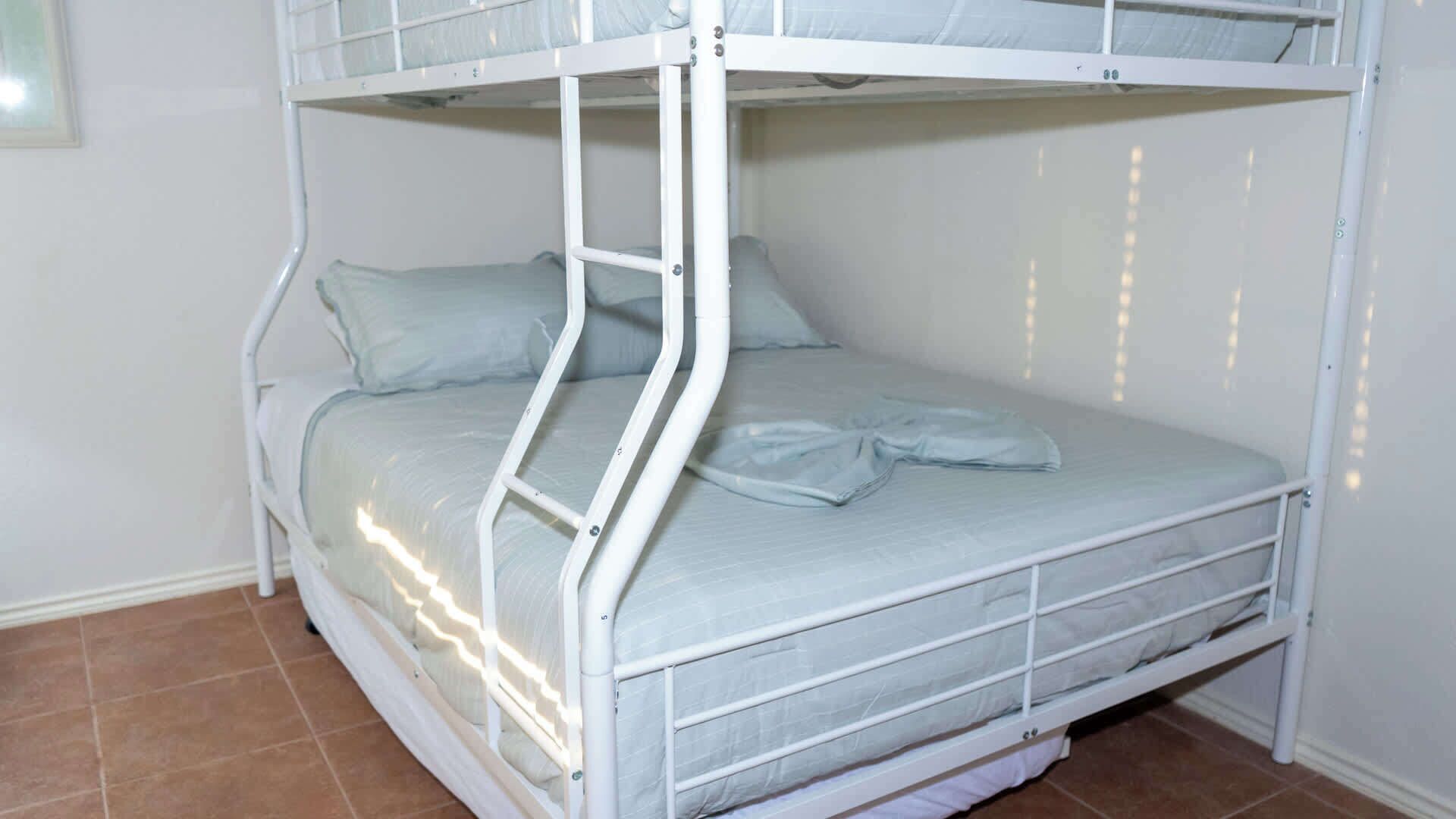 A bunk bed with a ladder, white walls, and tiled flooring.
