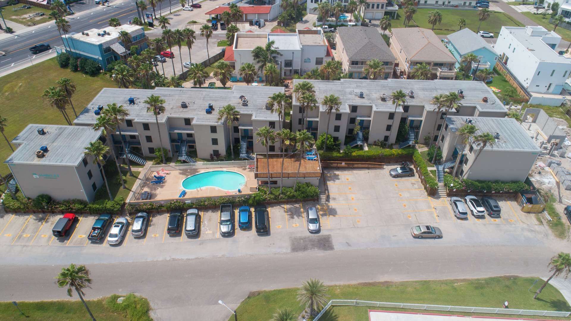 Vista aerea di un hotel a più piani con piscina, parcheggio e palme circostanti.