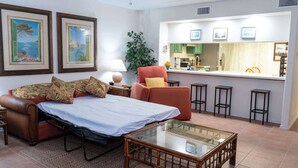 A living room with a sofa, a glass coffee table, a red armchair, and a kitchen area with stools. - Renovated 1st Floor Beach 250ft Pool (South Padre Island)