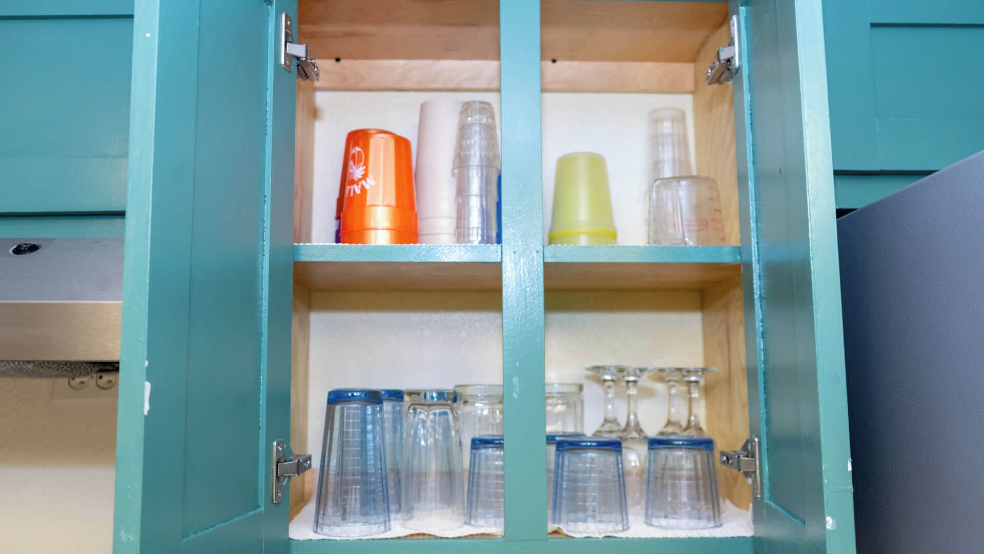 A teal cabinet with four shelves, each containing various glass containers and bottles.