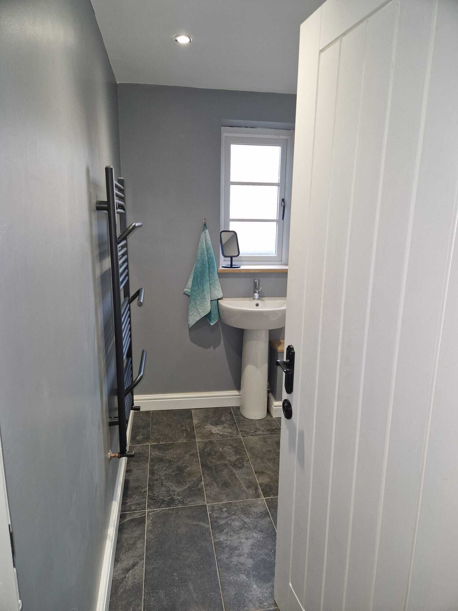 Une salle de bain avec un mur gris, un lavabo blanc, une fenêtre et un porte-serviettes.