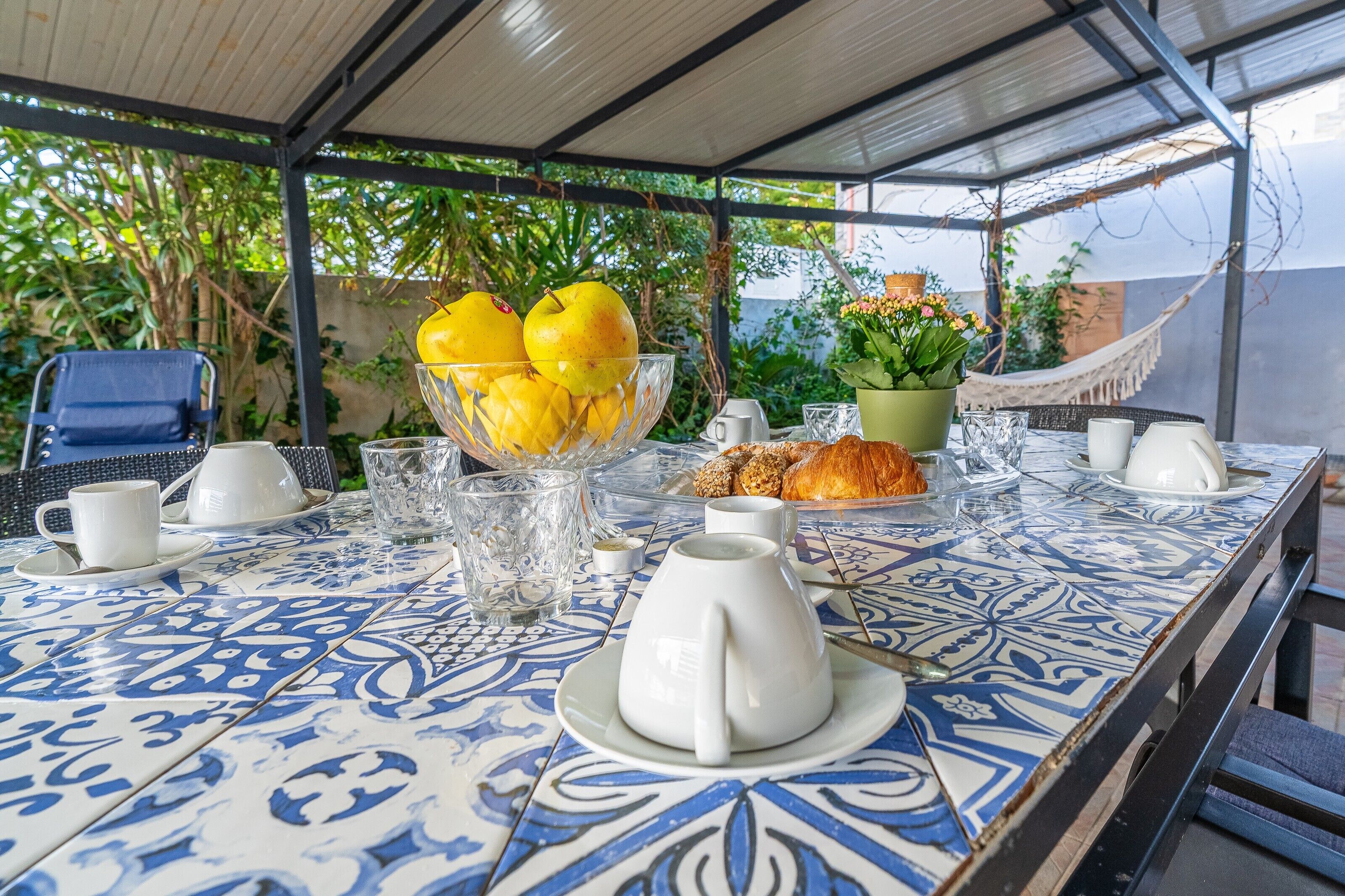Une table dressée avec des aliments pour le petit-déjeuner, un saladier de fruits et, au fond, un hamac.