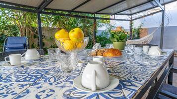 Une table dressée avec des aliments pour le petit-déjeuner, un saladier de fruits et, au fond, un hamac.