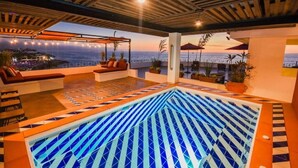 Une piscine sur le toit, agrémentée d’un motif géométrique en mosaïque, d’un espace salon extérieur et offrant une vue sur l’océan.