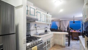 Une cuisine moderne équipée d’une cuisinière, d’un four et d’un évier, un coin repas avec une table et des chaises, et une vue sur le ciel par la fenêtre.