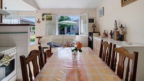 A dining area with a table, chairs, a vase with flowers, a kitchen with an oven, and a view of the outdoors. - Gîte la Cache-maille in Bias (Bias)