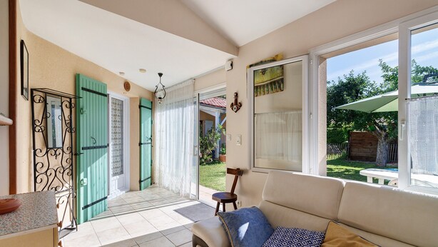A living room with a sofa, a dining table, and a kitchen area with a door and window. - Gîte la Cache-maille in Bias (Bias)