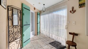 A hallway with patterned tiles, a wooden chair, a decorative metal gate, and a window with sheer curtains. - Gîte la Cache-maille in Bias (Bias)