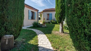 A pathway leading to a building with a tiled roof and blue shutters, surrounded by neatly trimmed hedges. - Gîte la Cache-maille in Bias (Bias)