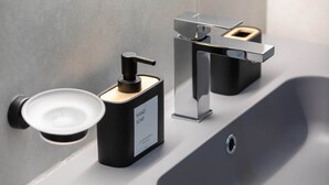 Et moderne badeværelse med en sort sæbedispenser, en kromarmatur og et rektangulært spejl.