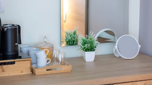 Een houten bureau met een koffiezetapparaat, kopjes, glazen, een dienblad, een potplant en een spiegel.
