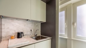 Una cocina moderna con un lavamanos de acero inoxidable, una tetera eléctrica negra y una encimera de mármol.