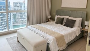 A modern bedroom with a large bed, a bench, a nightstand, and a view of a cityscape through a large window. - Relaxing 2BR Apartment in Al Bateen JBR - Walk to Beach & The Walk (Dubai)