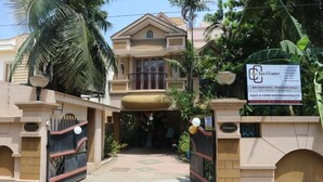 A hotel entrance with a gated driveway, palm trees, and a sign for Eaze & Comfort Hospitality. - Eaze & Comfort - Boutique Hotel (Chennai)