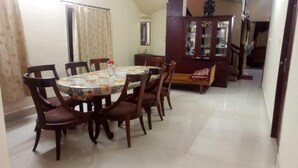 A dining area with a round table and six chairs, a wooden cabinet with glass doors, and a red sofa. - Eaze & Comfort - Boutique Hotel (Chennai)