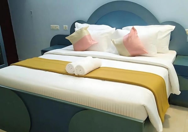 A neatly made bed with white and yellow bedding, a blue headboard, and a bedside table with a lamp.