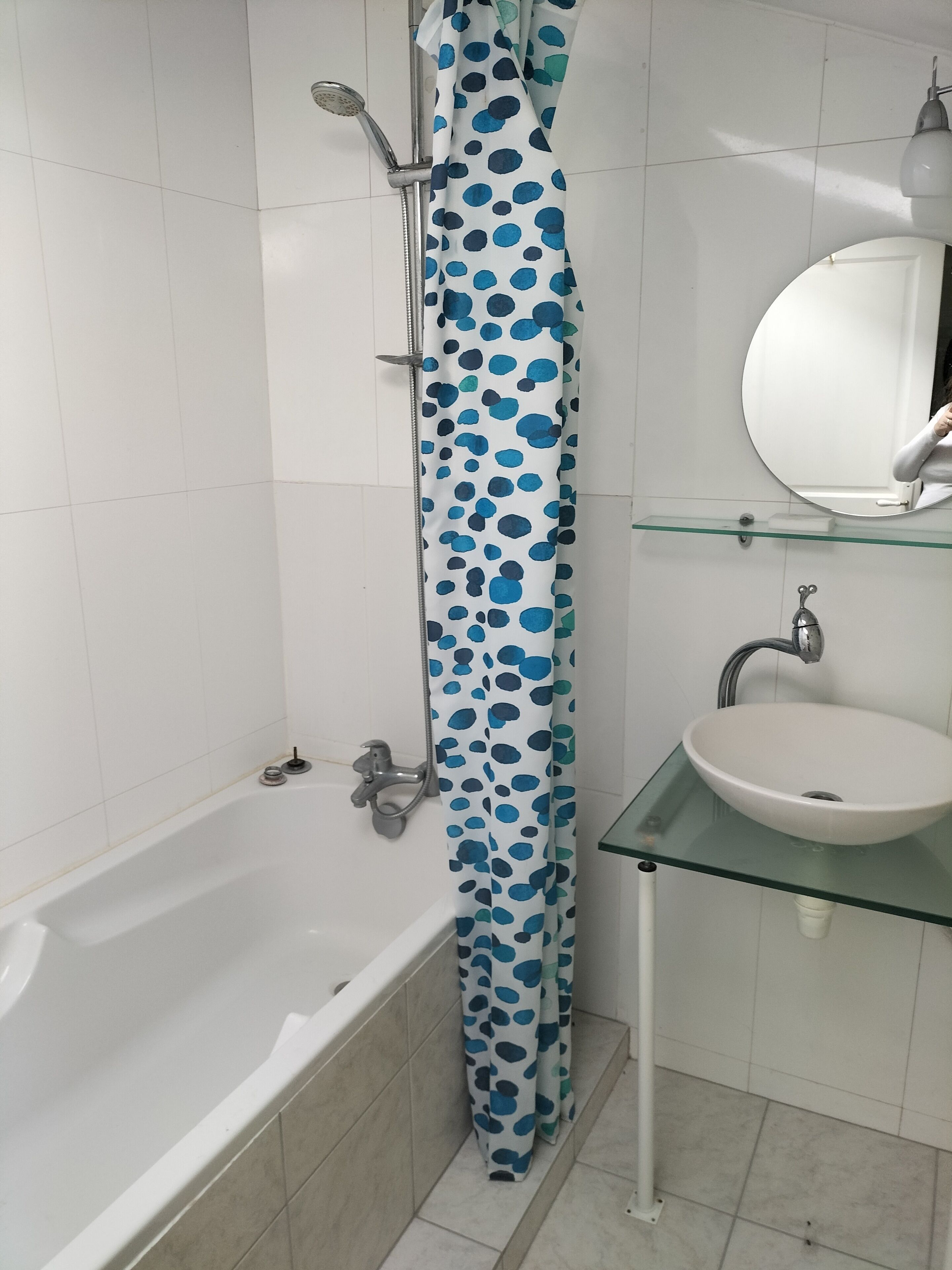 A bathroom with a bathtub, a glass sink, and a shower curtain with a blue polka dot pattern.