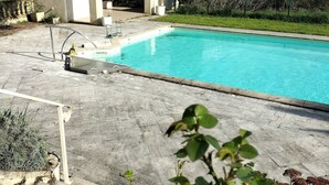 A swimming pool with a tiled deck, a pergola, and a view of the countryside.