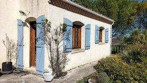 A building with blue shutters and a tiled roof, surrounded by greenery and a clear sky.