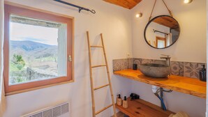 Ein Badezimmer mit einer Holzlader, einem großen Fenster mit Blick, einem runden Spiegel und einem Holzboden mit einem Steintonne.
