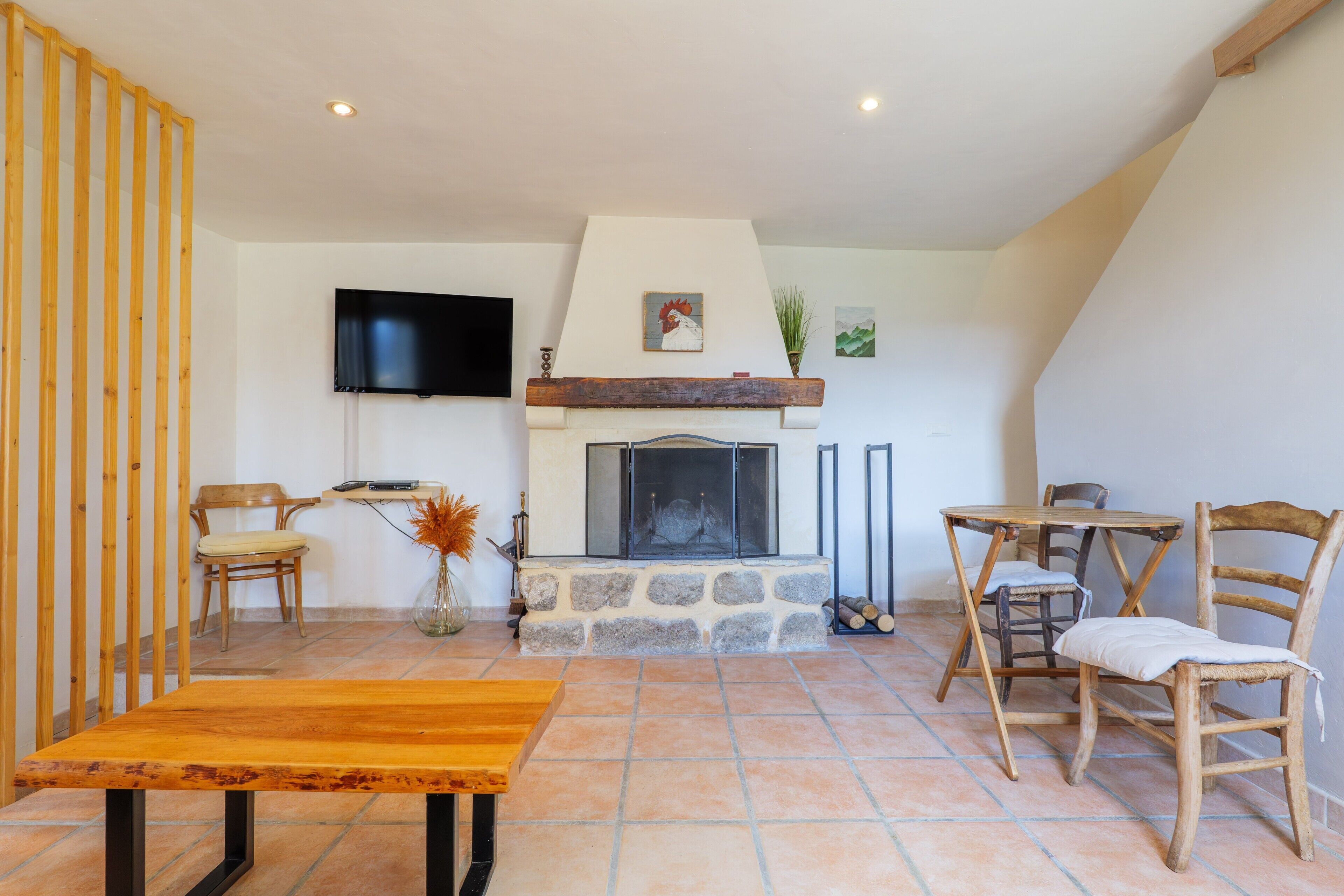 A cozy living room with a fireplace, a TV mounted on the wall, and a dining area with chairs and a table.