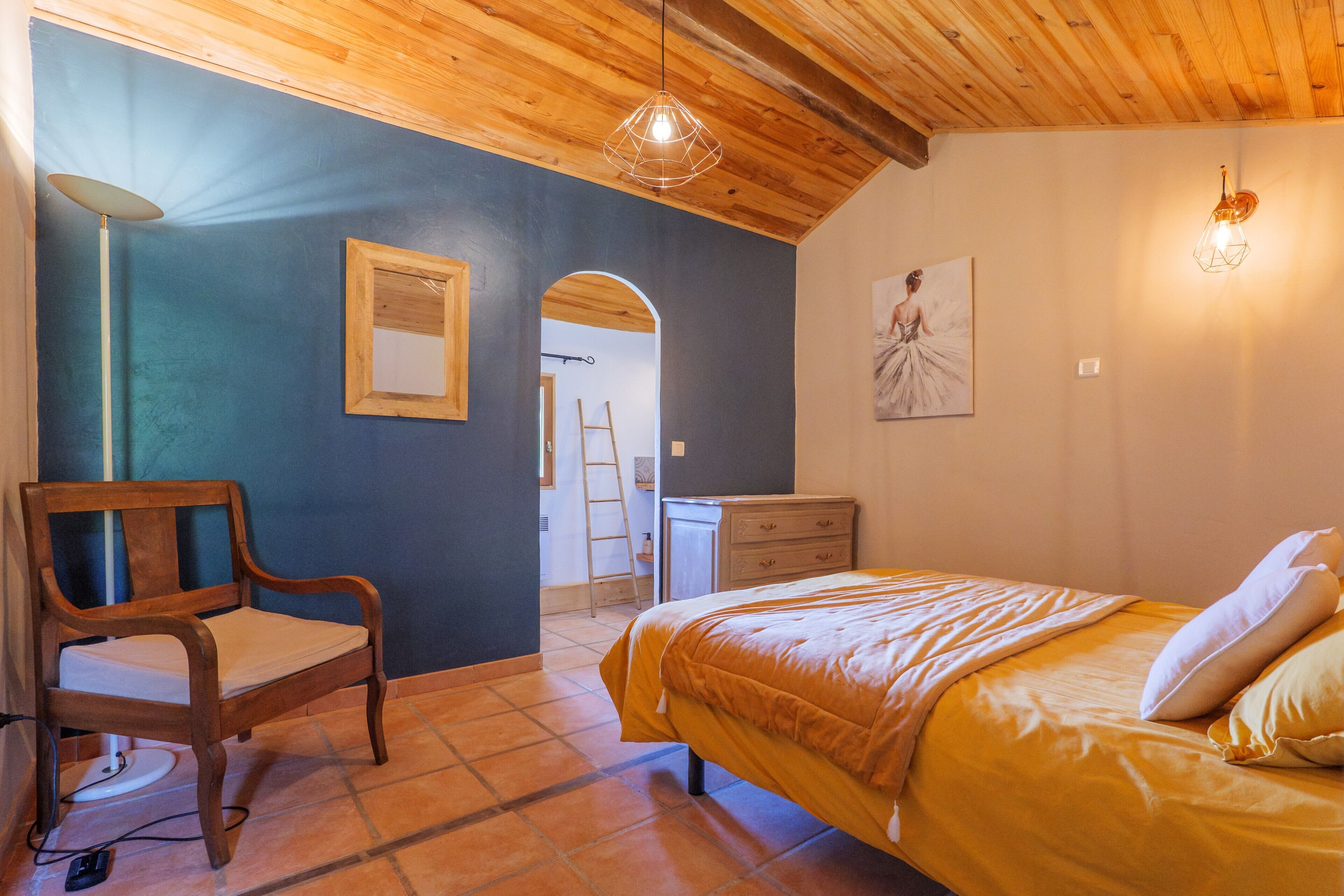 Une chambre à coucher avec un lit, une chaise, une commode, une lampe et un tableau au mur.