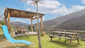Eine hölzerne Laube mit Tisch und Stühlen, ein blauer Liegestuhl und ein Picknicktisch.