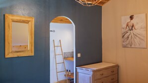 Ein Zimmer mit Holzbalkendecke, einem Spiegel, einer Leiter, einem Schmuckkästchen und einem Gemälde.