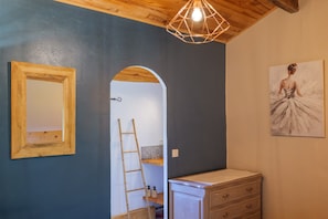Ein Zimmer mit Holzbalkendecke, einem Spiegel, einer Leiter, einem Schmuckkästchen und einem Gemälde.