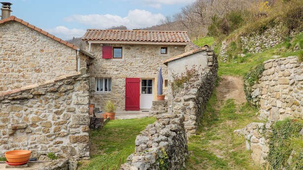 Ein Steinhaus mit roter Tür, einem kleinen Garten und einer Steinmauer.