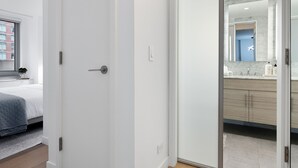 Een moderne slaapkamer met een bed, een witte deur en uitzicht op een badkamer met een spiegel en wastafel.