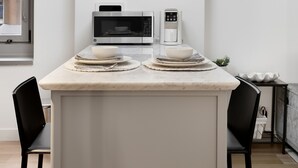 Een moderne keuken met een marmeren aanrecht, zwarte stoelen, een koffiezetapparaat en een magnetron.