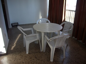 A room with a round table and four white chairs, a window with curtains, and a door leading outside. - Islandia 15C in Benidorm (Benidorm)