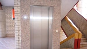 An elevator with a metallic door, a fire extinguisher on the wall, and a staircase with wooden steps and red accents. - LAS Tejas 2-31 in Benidorm (Benidorm)