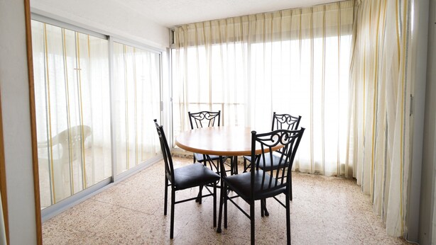 A dining area with a round table and four chairs, large windows with curtains, and a tiled floor. - Caballos 14H in Benidorm (Benidorm)