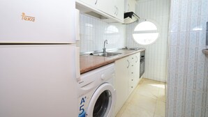 A compact kitchen with white cabinets, a washing machine, a sink, and a window. - Caballos 14H in Benidorm (Benidorm)