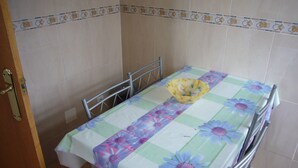 Un petit coin repas avec une table recouverte d’une nappe à motifs floraux, une chaise en métal et un banc en métal.