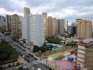 A high-rise building with multiple floors, surrounded by other buildings, a parking area, and a playground with a blue pool. - Eden Park 8C in Benidorm (Benidorm)