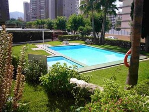 A rectangular swimming pool surrounded by well-maintained grass and shrubs, with a lifebuoy hanging on a tree nearby. - Eden Park 8C in Benidorm (Benidorm)