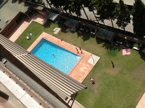 Vista aérea de uma piscina cercada por gramado, cadeiras de descanso e guarda-sóis.