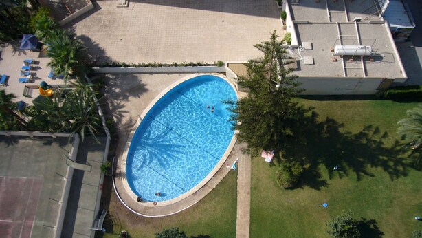 Vista aérea de una piscina rodeada de césped, con un edificio al fondo.
