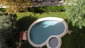 Eine Vogelperspektive auf einen Pool mit ungewöhnlicher Form, umgeben von gepflegten Rasenflächen und Bäumen.